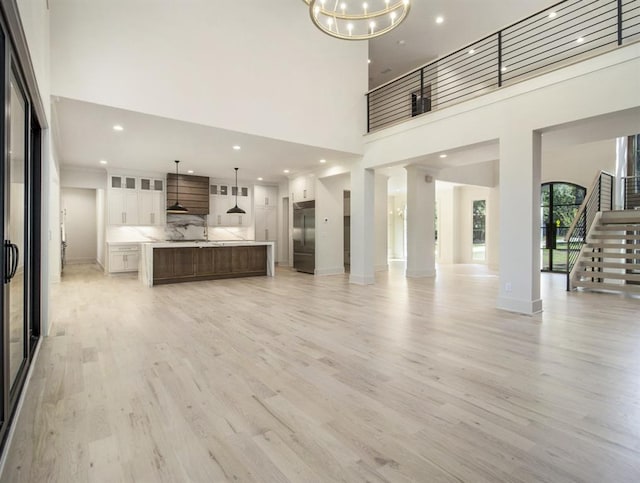 unfurnished living room featuring a notable chandelier, a high ceiling, and light wood-type flooring