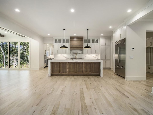 kitchen with stainless steel built in refrigerator, pendant lighting, tasteful backsplash, a large island with sink, and light wood-type flooring