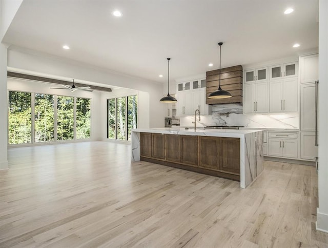 kitchen featuring a spacious island, white cabinets, light wood-type flooring, and tasteful backsplash