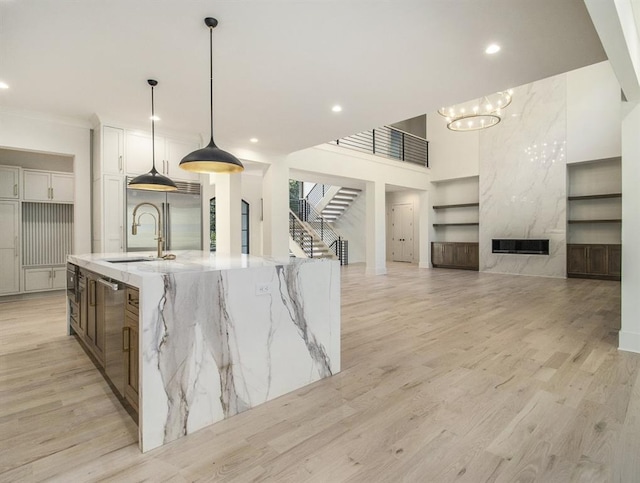 kitchen featuring a large island, pendant lighting, light wood-type flooring, white cabinets, and light stone countertops