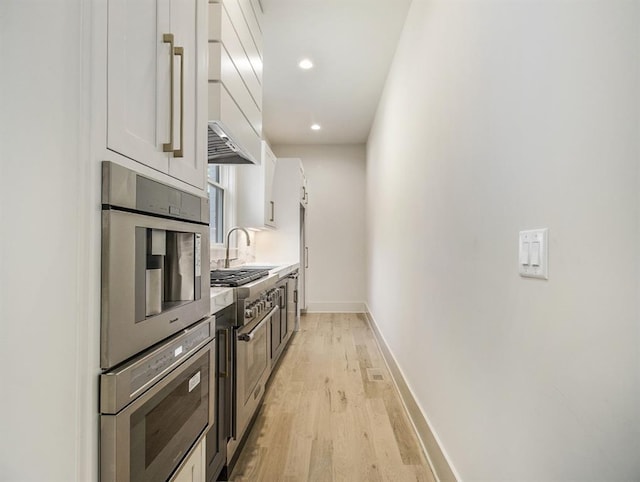 kitchen with white cabinets, oven, light wood-type flooring, and sink