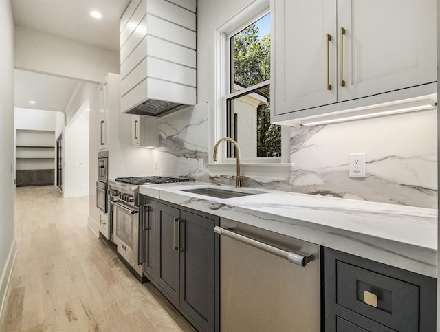 kitchen with sink, decorative backsplash, light hardwood / wood-style flooring, appliances with stainless steel finishes, and premium range hood