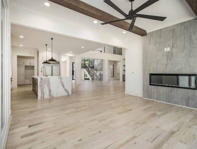 unfurnished living room with ceiling fan, light wood-type flooring, beam ceiling, and sink