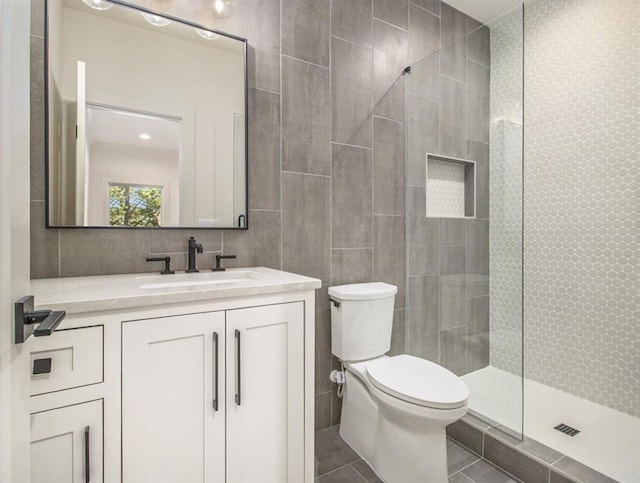 bathroom with tile walls, tiled shower, vanity, and toilet