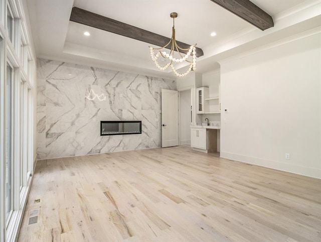 unfurnished living room featuring beamed ceiling, a raised ceiling, light hardwood / wood-style flooring, a notable chandelier, and a fireplace