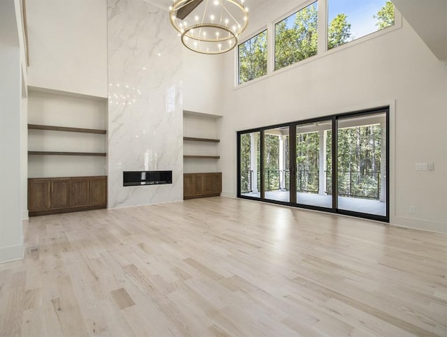 unfurnished living room featuring a towering ceiling, a high end fireplace, and light wood-type flooring