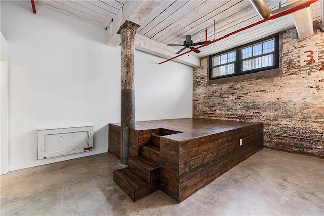 basement featuring ceiling fan, wooden ceiling, and brick wall