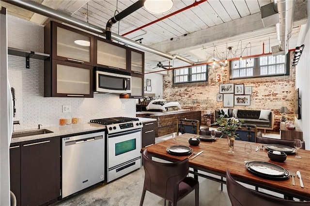 kitchen featuring brick wall, dark brown cabinetry, appliances with stainless steel finishes, ceiling fan, and sink