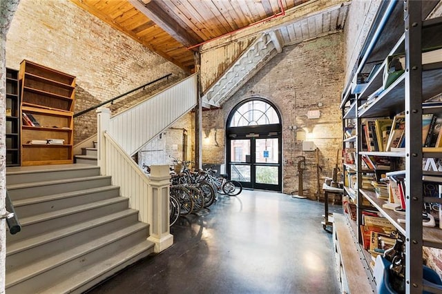 foyer entrance featuring brick wall, french doors, a towering ceiling, beam ceiling, and wooden ceiling