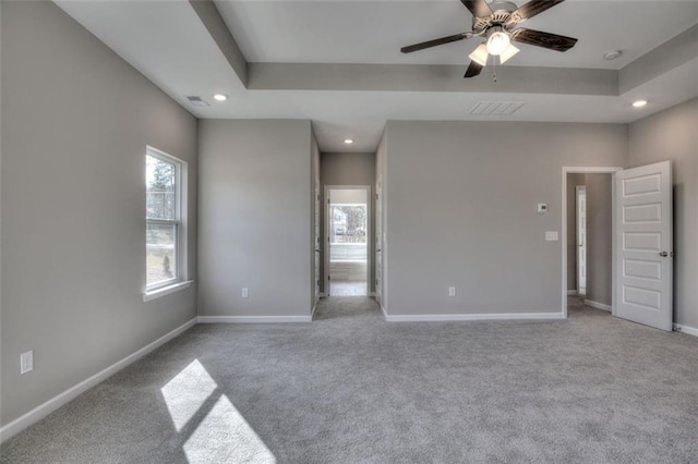 unfurnished bedroom with multiple windows, light carpet, recessed lighting, baseboards, and a tray ceiling