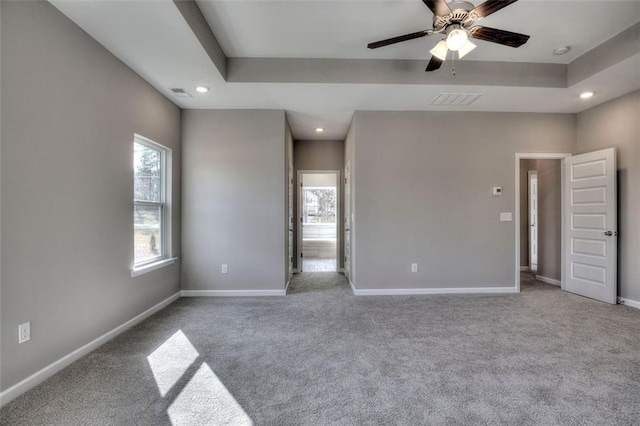 unfurnished bedroom featuring multiple windows, recessed lighting, carpet, baseboards, and a tray ceiling