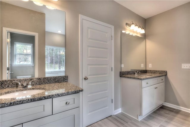 bathroom with baseboards, two vanities, and toilet