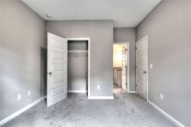 unfurnished bedroom featuring light colored carpet, baseboards, a closet, and ensuite bath