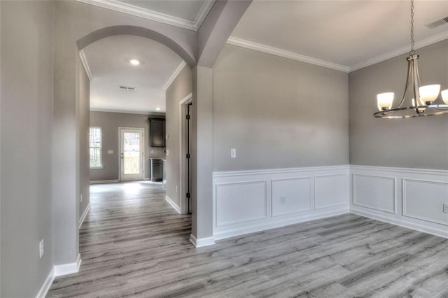 unfurnished dining area featuring arched walkways, light wood-type flooring, a chandelier, ornamental molding, and baseboards
