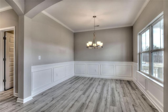 unfurnished dining area featuring plenty of natural light, light wood-style flooring, ornamental molding, a chandelier, and arched walkways