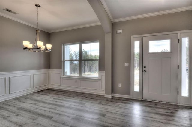 foyer entrance featuring ornamental molding, a chandelier, wood finished floors, and wainscoting