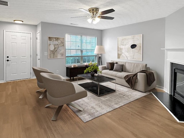 living area featuring a glass covered fireplace, visible vents, a textured ceiling, and wood finished floors