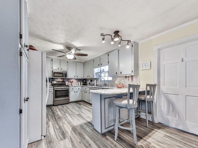 kitchen with stainless steel appliances, a kitchen breakfast bar, kitchen peninsula, and light hardwood / wood-style floors