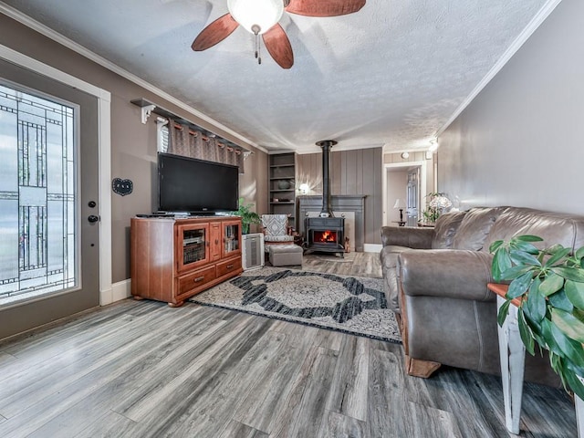 living room featuring a wood stove, hardwood / wood-style flooring, ornamental molding, ceiling fan, and a textured ceiling