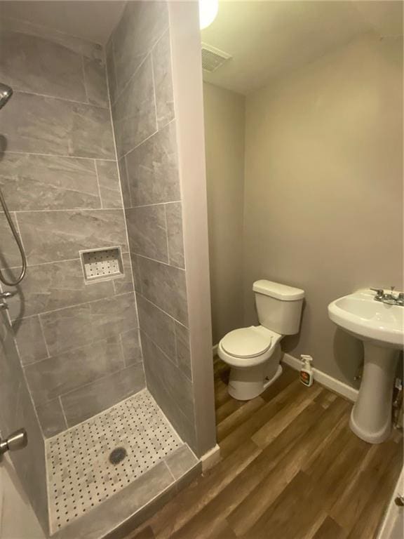 bathroom featuring a tile shower, hardwood / wood-style floors, and toilet