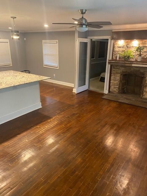 unfurnished living room featuring a stone fireplace, dark wood-type flooring, and ceiling fan