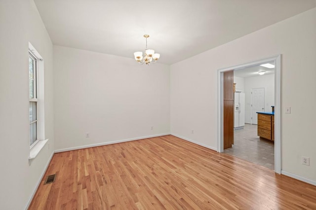 empty room with light wood-type flooring and a chandelier