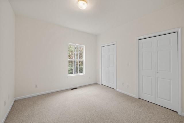 unfurnished bedroom with multiple closets and light carpet