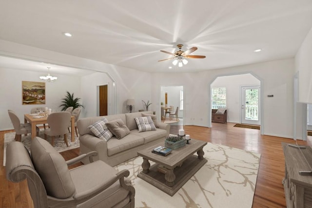 living room featuring ceiling fan with notable chandelier and light hardwood / wood-style flooring