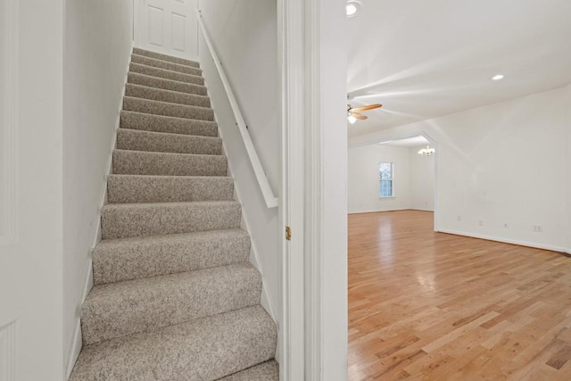 staircase featuring wood-type flooring and ceiling fan with notable chandelier