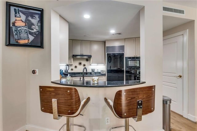 kitchen featuring black appliances, a kitchen breakfast bar, gray cabinetry, and light hardwood / wood-style flooring