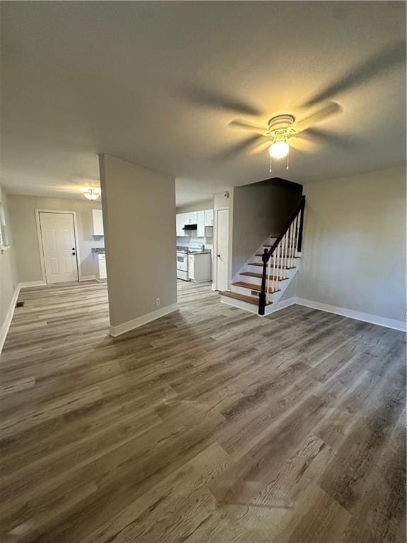 unfurnished living room with stairs, dark wood finished floors, baseboards, and ceiling fan