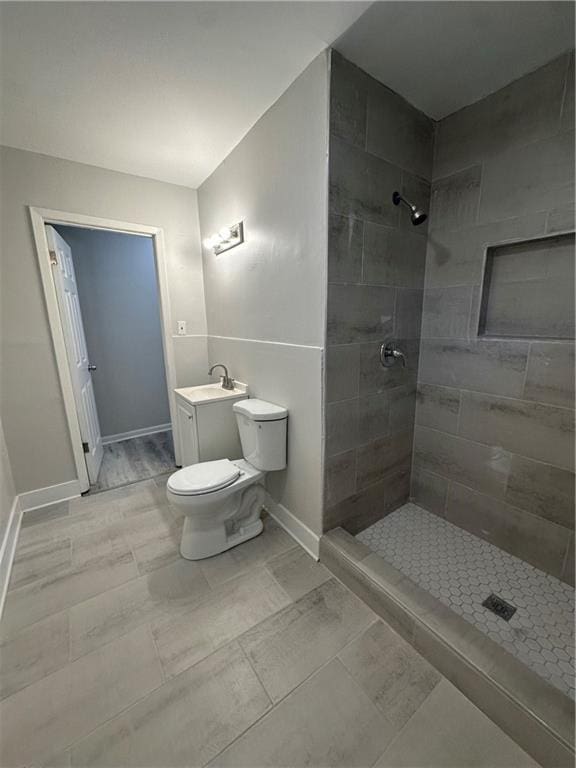 full bath with a tile shower, toilet, vanity, and baseboards