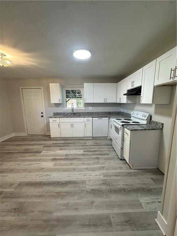 kitchen featuring white appliances, a sink, white cabinets, under cabinet range hood, and dark countertops