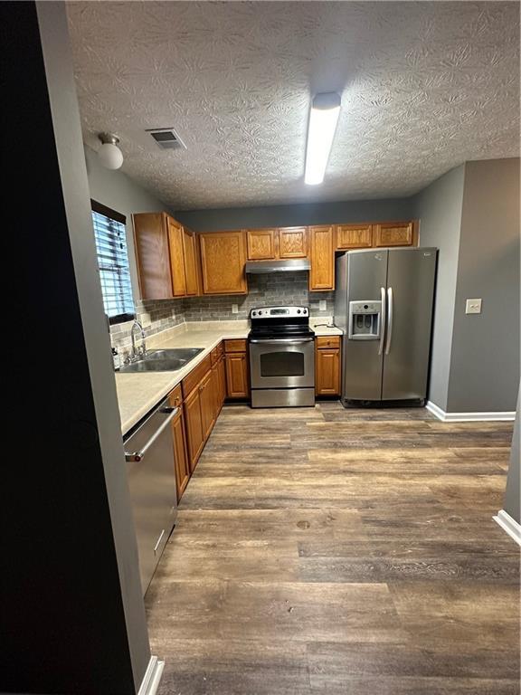 5768 Windgate Ln, Lithonia, GA 30058 - kitchen with stainless steel appliances, under cabinet range hood, light countertops, wood finished floors, and brown cabinetry
