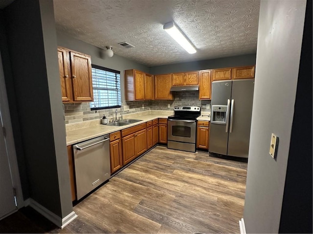 5768 Windgate Ln, Lithonia, GA 30058 - kitchen featuring appliances with stainless steel finishes, under cabinet range hood, light countertops, tasteful backsplash, and wood finished floors