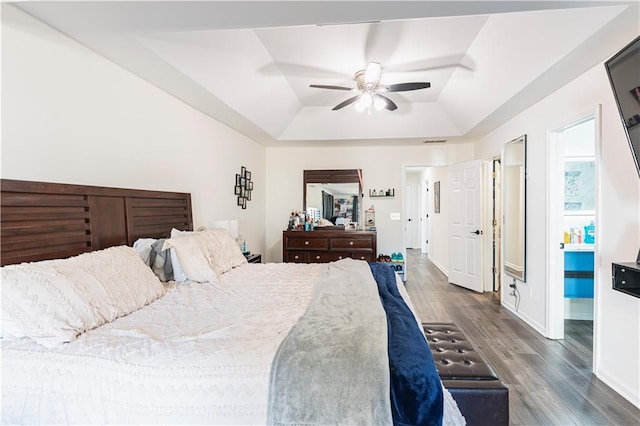 bedroom with a tray ceiling, visible vents, a ceiling fan, wood finished floors, and baseboards