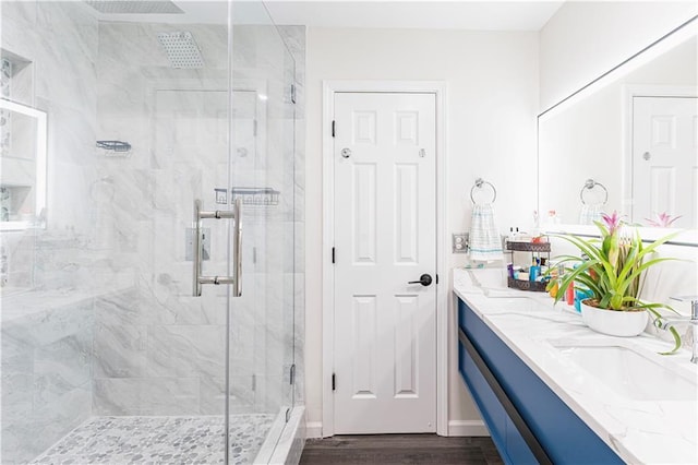 full bath with double vanity, a sink, a marble finish shower, and wood finished floors