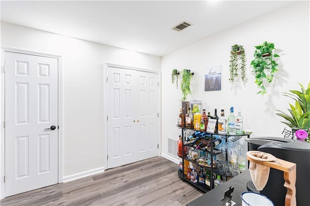 bar with a bar, baseboards, visible vents, and wood finished floors