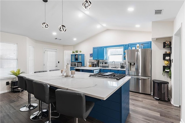 kitchen with wood finished floors, blue cabinetry, stainless steel fridge, and visible vents