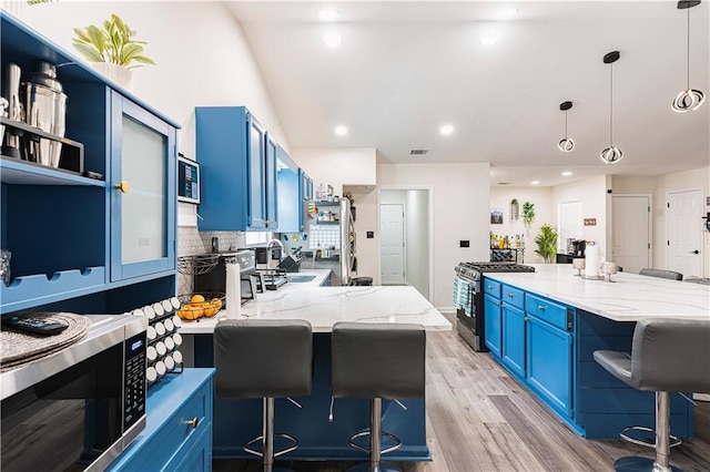 kitchen with light wood finished floors, open shelves, stainless steel appliances, blue cabinetry, and a kitchen bar