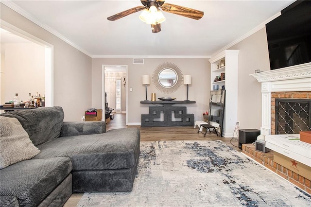 living room featuring crown molding, a fireplace, ceiling fan, and light wood-type flooring