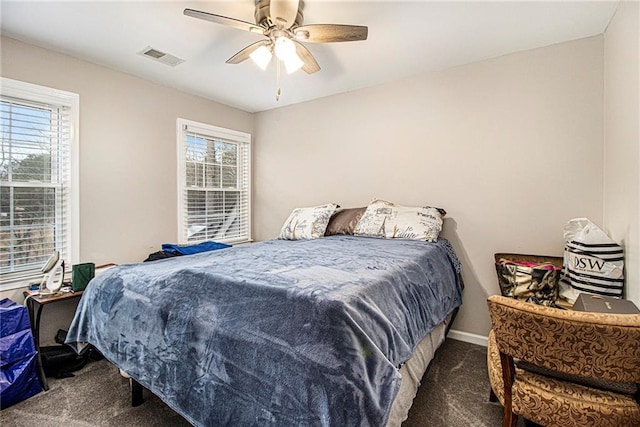 bedroom with multiple windows, dark colored carpet, and ceiling fan