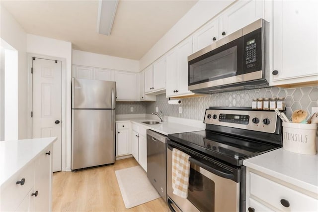 kitchen with light wood-type flooring, stainless steel appliances, white cabinets, light countertops, and decorative backsplash