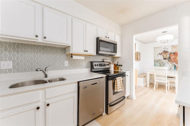 kitchen with backsplash, light countertops, white cabinets, stainless steel appliances, and a sink