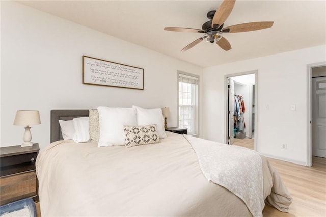 bedroom with a walk in closet, ceiling fan, baseboards, light wood-type flooring, and a closet