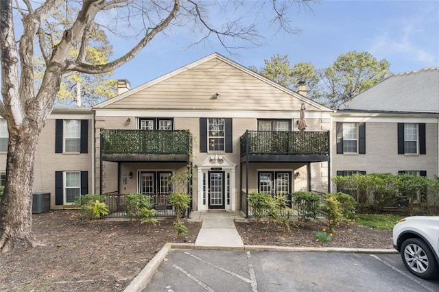 view of front of property featuring uncovered parking, a chimney, french doors, central air condition unit, and brick siding