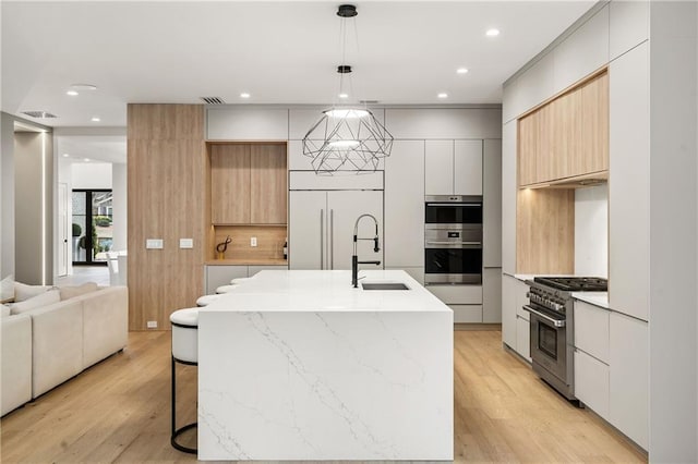 kitchen with sink, light hardwood / wood-style flooring, hanging light fixtures, premium appliances, and a center island with sink