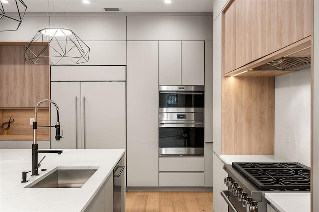 kitchen with sink, white cabinetry, stainless steel appliances, light hardwood / wood-style floors, and light stone countertops