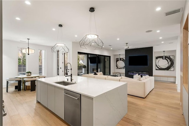 kitchen with sink, a kitchen island with sink, white cabinetry, light hardwood / wood-style floors, and decorative light fixtures