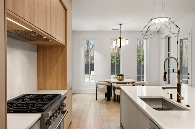 kitchen with pendant lighting, sink, light stone counters, stainless steel range, and light hardwood / wood-style floors